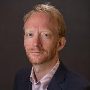 Man with reddish hair and blazer looking at camera