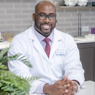 man wearing a lab coat, glasses, and smiling in a research lab setting