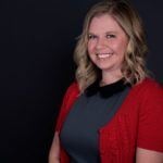 Portrait of a smiling woman with red sweater, dark grey shirt, and blond hair.