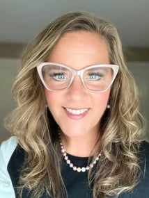 woman looking into camera, wearing glasses, pearl necklace, and curled hair
