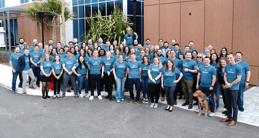 Large group of people in matching blue t-shirts standing outside a building and smiling