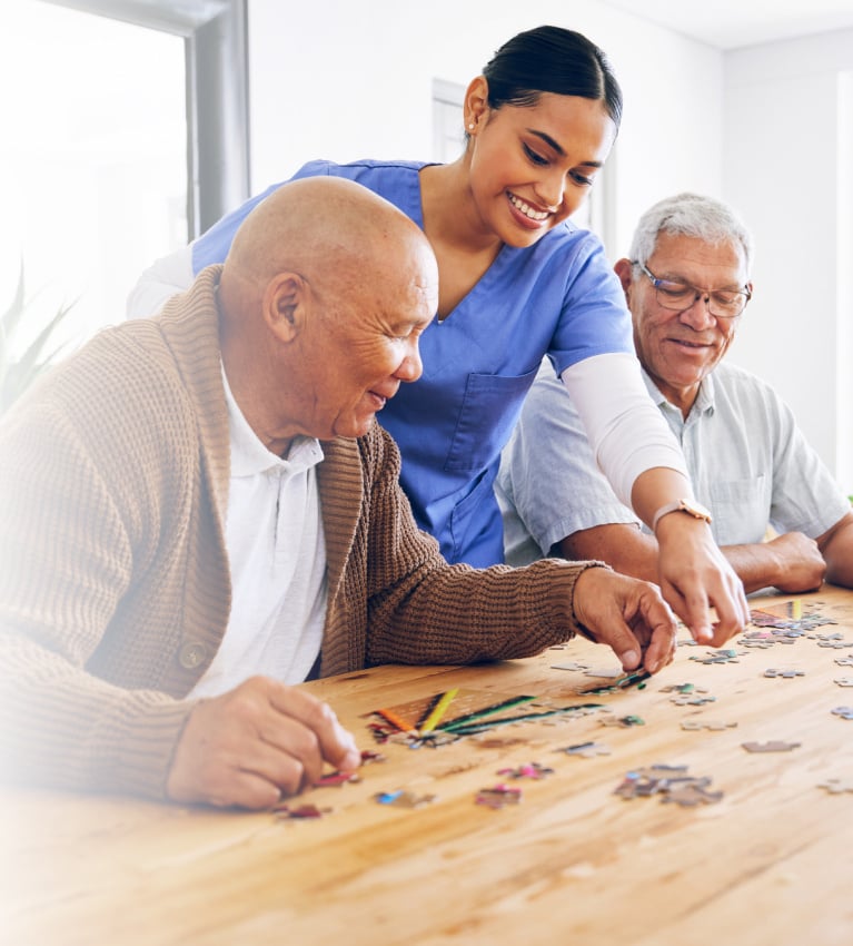 Young woman in scrubs helping two senior men with a puzzle